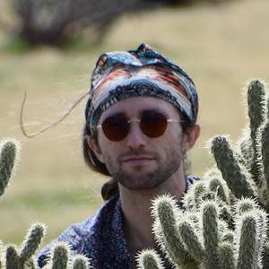 Closeup of Dillion Jones behind cacti outside.