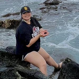 Jenna Luc sitting on rocks with ocean below and behind her.